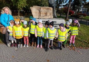 Dzieci z nauczycielką stoją przed pomnikiem Rafała Bartoszewskiego w Aleksandrowie Łódzkim.